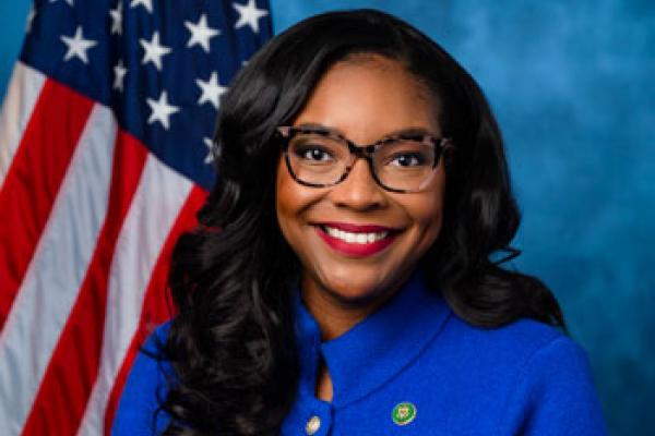 African-American woman with glasses wearing a blue suit posing with US flag in background