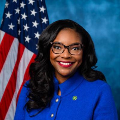 African-American woman with glasses wearing a blue suit posing with US flag in background